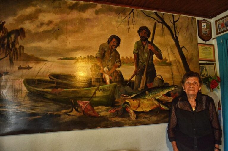 Dominga y una pintura que refleja su historia de vida vinculada a las aguas de los ríos. José Prinsich