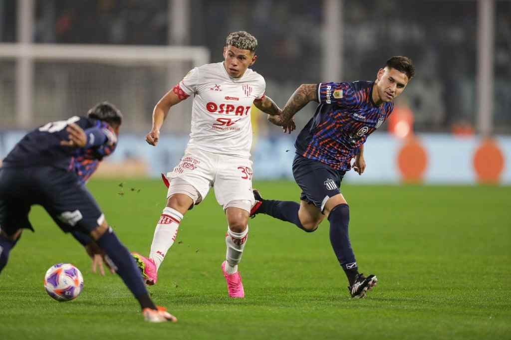 Imanol Machuca toca la pelota asediado por dos jugadores de Talleres. Ariel Carreras.