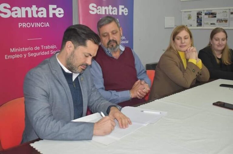 El ministro Báscolo firma ante la atenta mirada de Ramírez